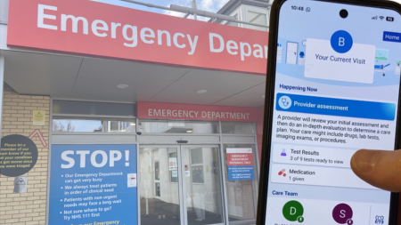 A mobile phone displaying the Bedside function of MyFrimleyHealth Record overlaid over an image of the netrance to the Emergency Department at Frimley Park Hospital