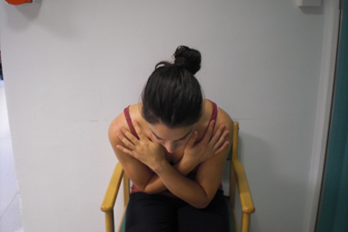 Person seated, bending torso forwards with hands crossed across chest.