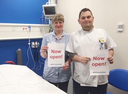 two members of staff hold up 'now open' signs celebrating the new building being open